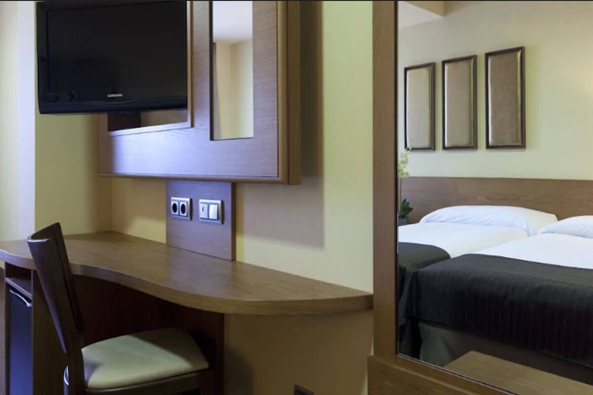 Habitación de hotel con escritorio, silla, televisor y cama con dos almohadas y una manta.