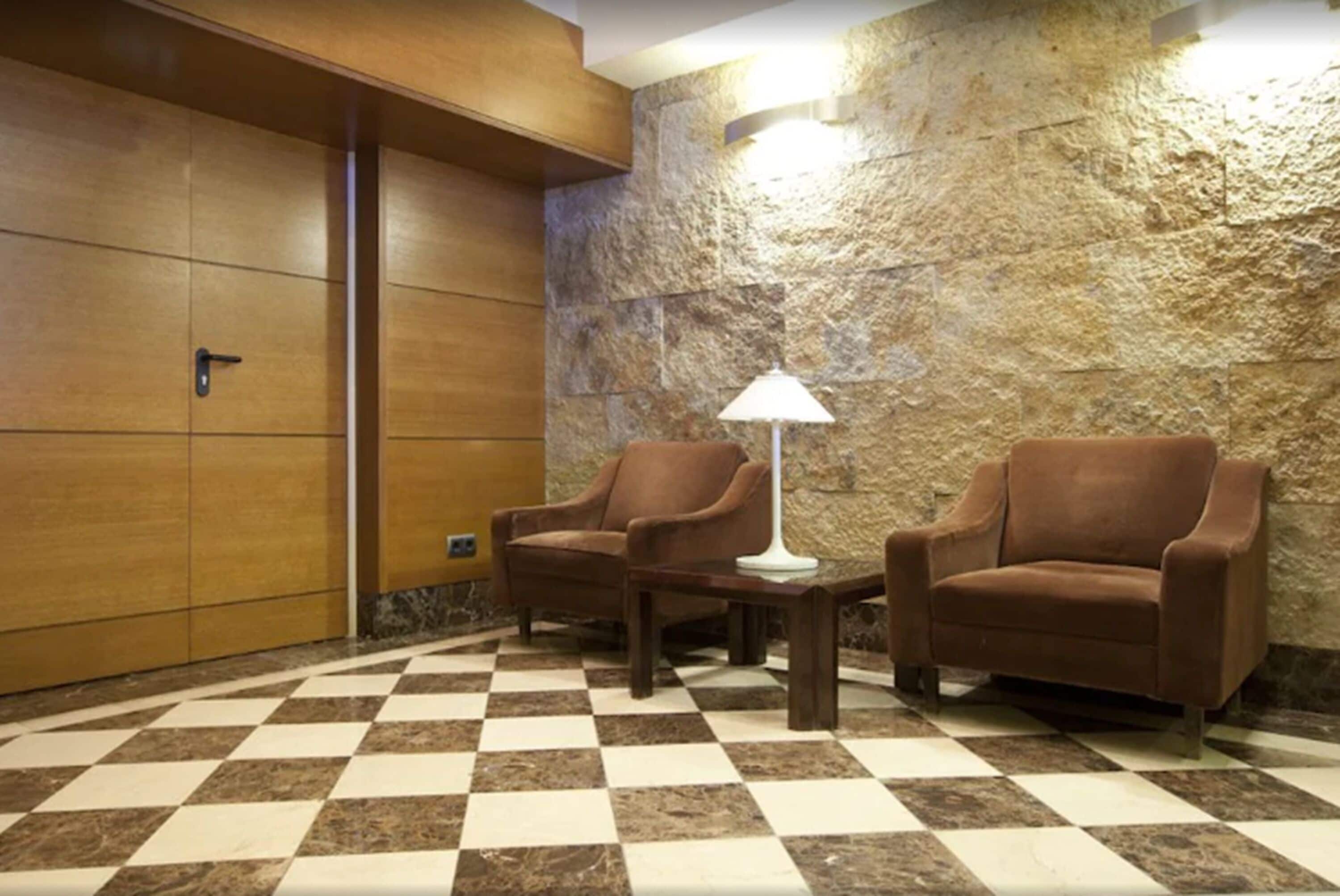 Un sol à carreaux, deux fauteuils marron, une lampe et une armoire en bois.