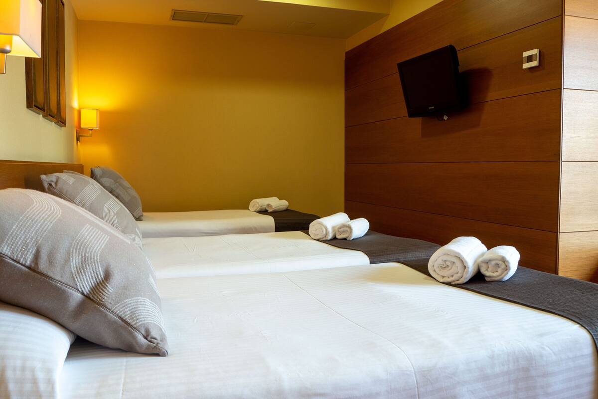 Habitación de hotel con dos camas, cada una con ropa blanca y toallas enrolladas. Hay un televisor de pantalla plana montado en la pared sobre las camas.