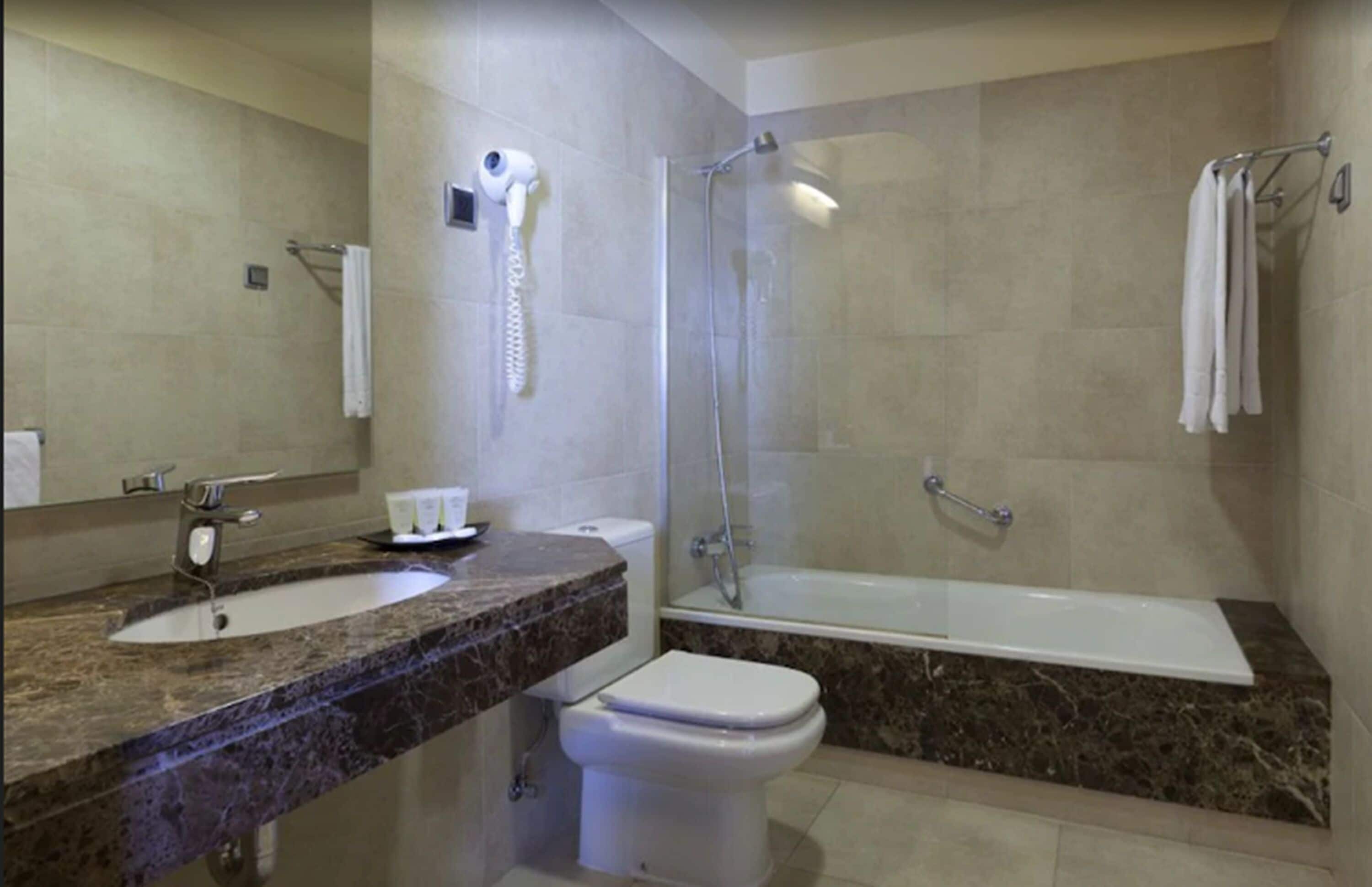 Ein Badezimmer mit Marmorwaschtisch, Toilette, Dusche mit Glastür und Badewanne.