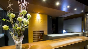 A reception desk with a vase of flowers, a clock on the wall, and a modern interior design. - Hotel America (Igualada)
