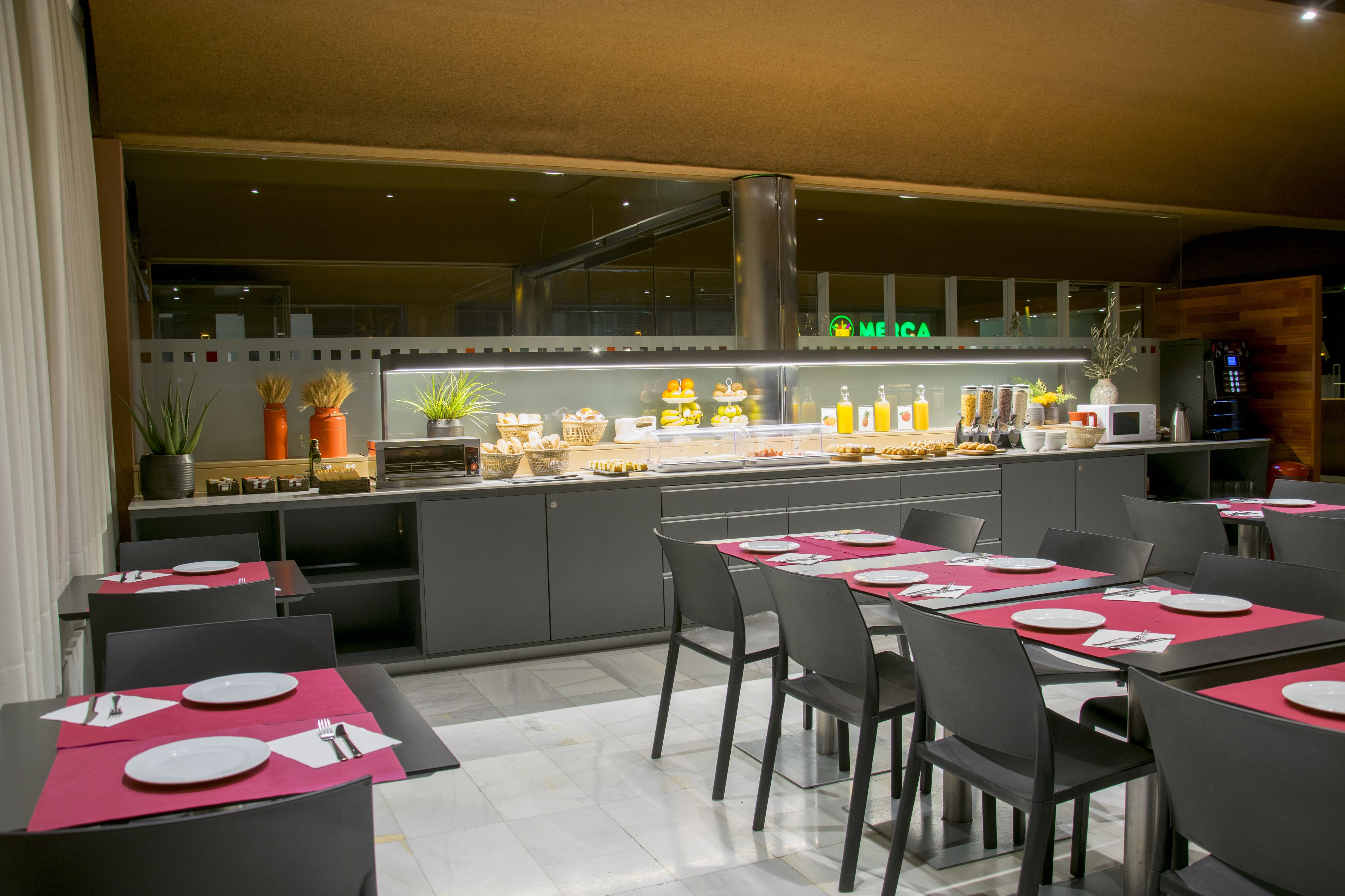 Un restaurante moderno con zona de bar, varias mesas con posavasos rosa y una variedad de exhibiciones de comida y bebidas.