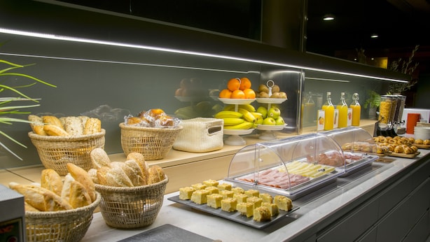 A buffet with various food items including bread, fruits, and pastries. - Hotel America (Igualada)