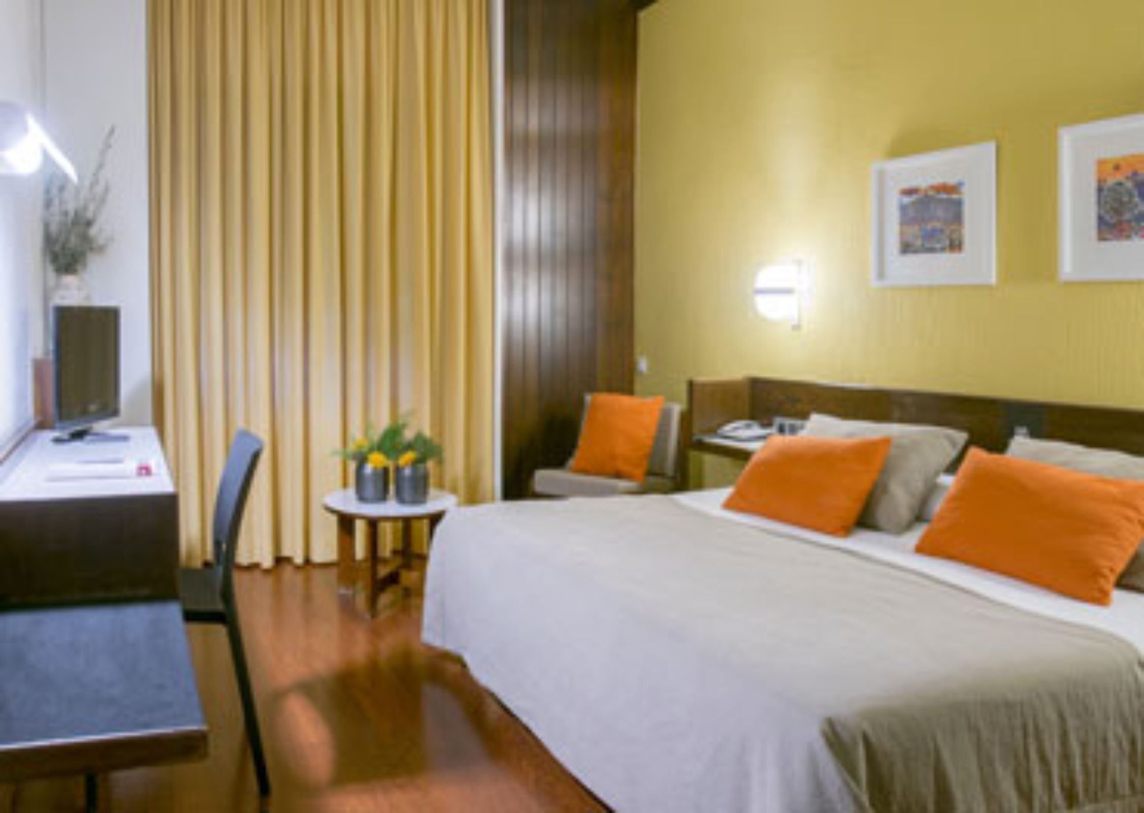 Ein Hotelzimmer mit Bett, Schreibtisch, Stuhl und einem kleinen Tisch mit Pflanze.