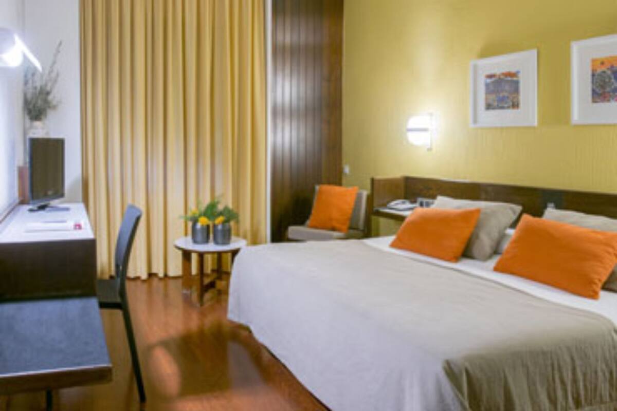 A hotel room with a bed, a desk, a chair, and a small table with a plant.