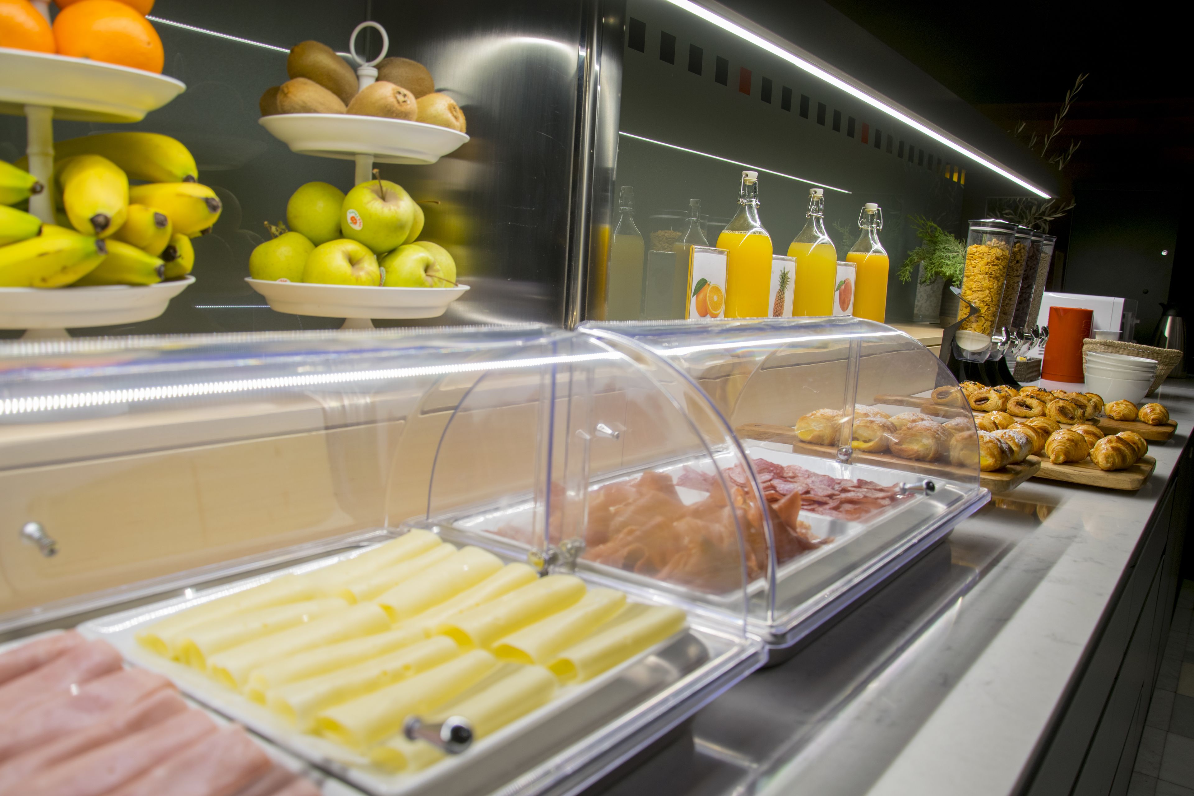 Un bufé con diversas opciones de comida, como frutas, bollería y bebidas.