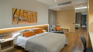A modern hotel room with a large bed, a bedside table, a chair, a mirror, and a painting of trees. - Hotel America (Igualada)