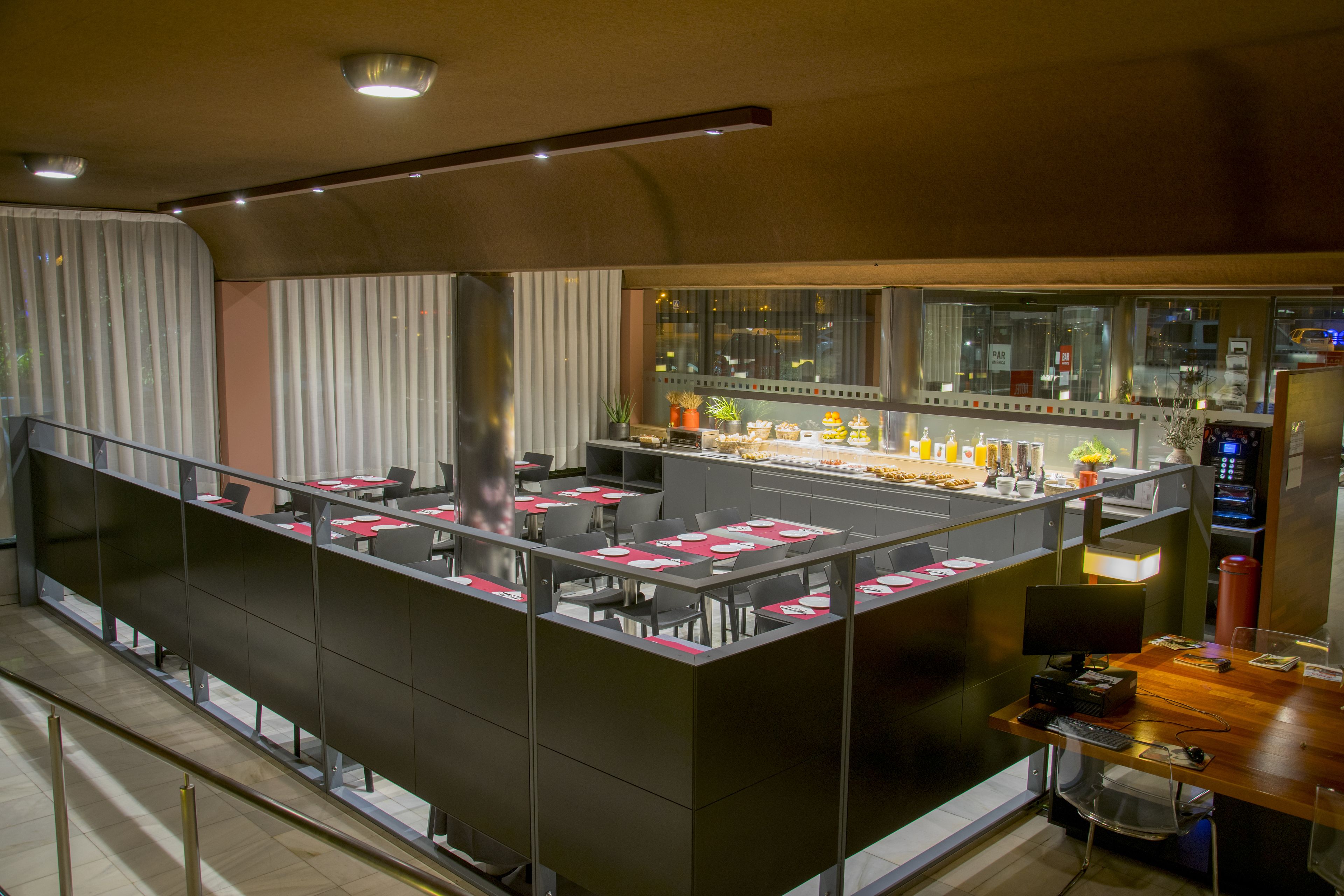 Un restaurant moderne avec un plafond haut, des cloisons en verre et un espace bar équipé d’un écran d’ordinateur.