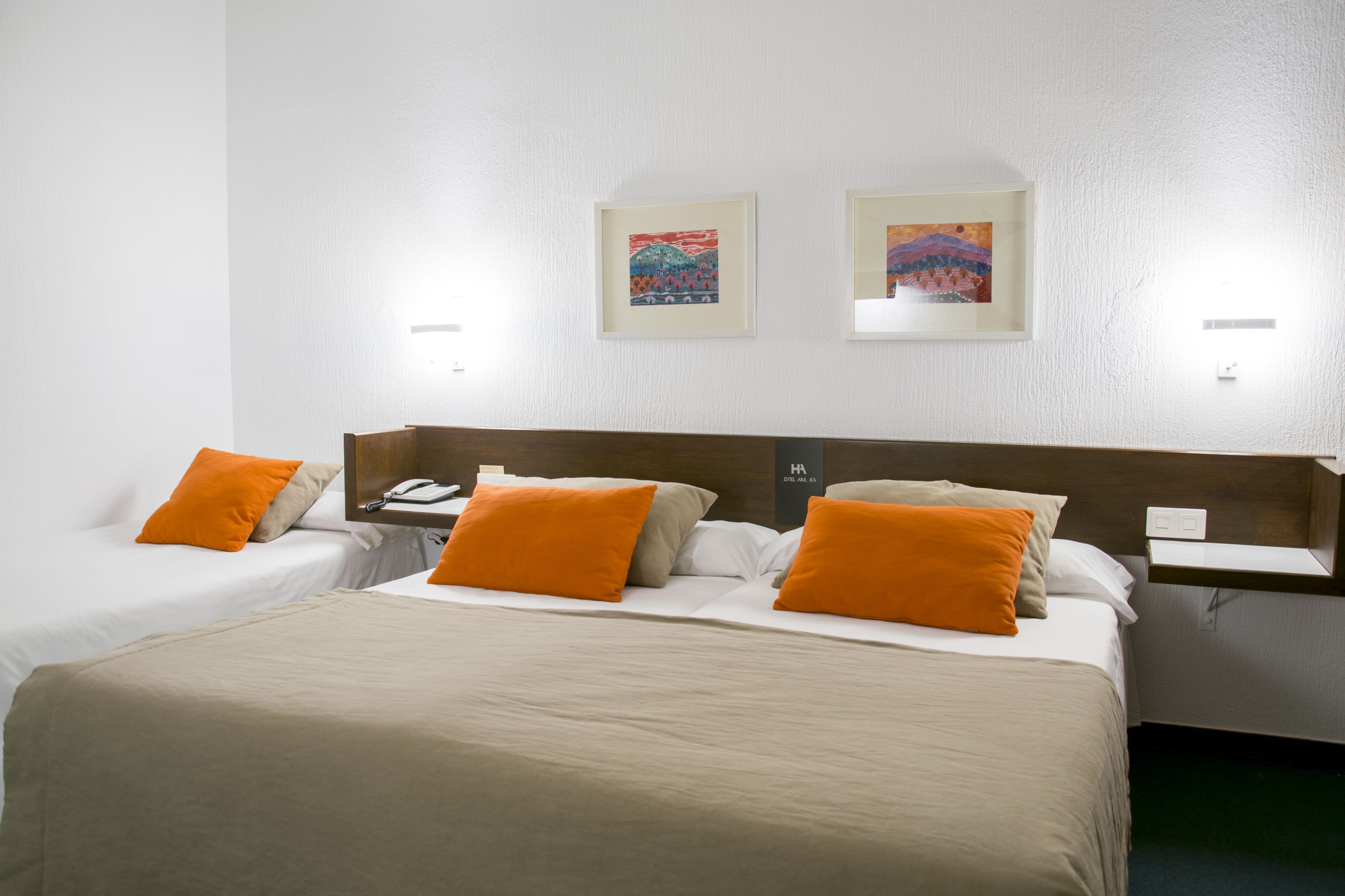 Ein Hotelzimmer mit zwei Betten, jeweils mit orangefarbenen Kissen, einem Holzkopfteil und Bildern an den Wänden.