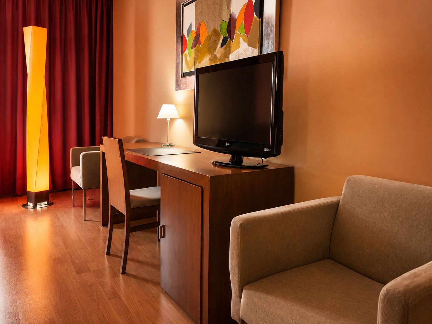 Hotelkamer met een houten bureau, een flatscreen-televisie, een lamp, een bank en een groot kunstwerk aan de muur.