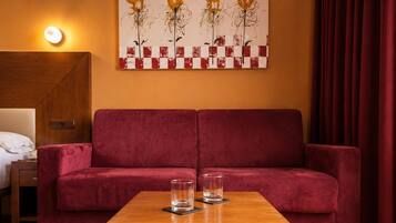 Un sofá rojo, una mesa de madera con dos vasos, y un cuadro en la pared.