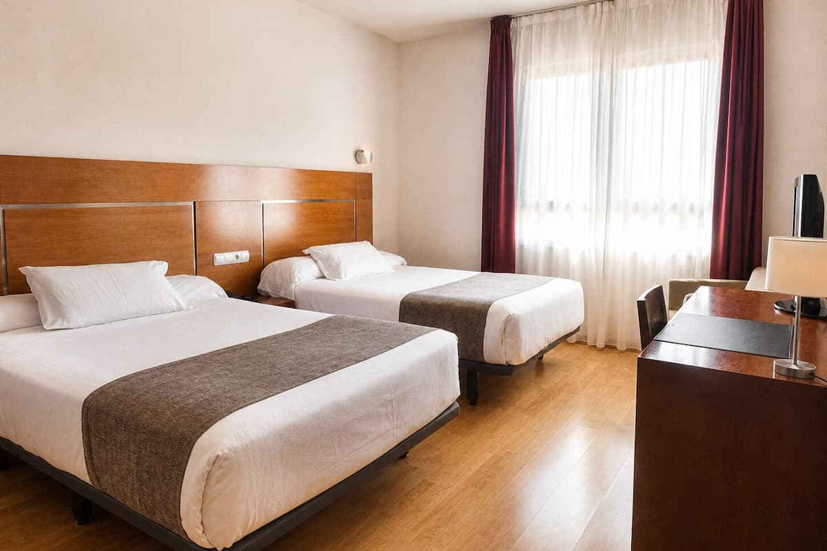 A hotel room with two beds, a desk, and a TV.