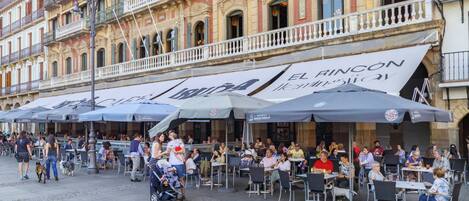 An outdoor café with outdoor seating and umbrellas, located in front of a building with ornate architecture.