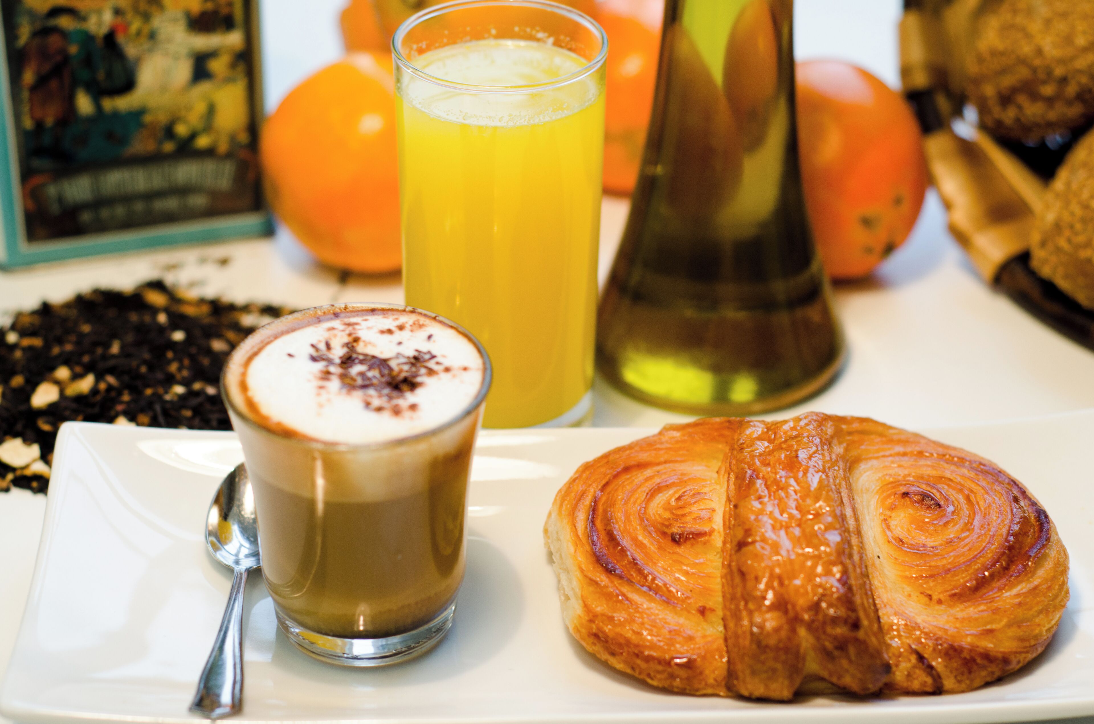 A plate with a croissant and a glass of orange juice, a spoon, and a bottle.