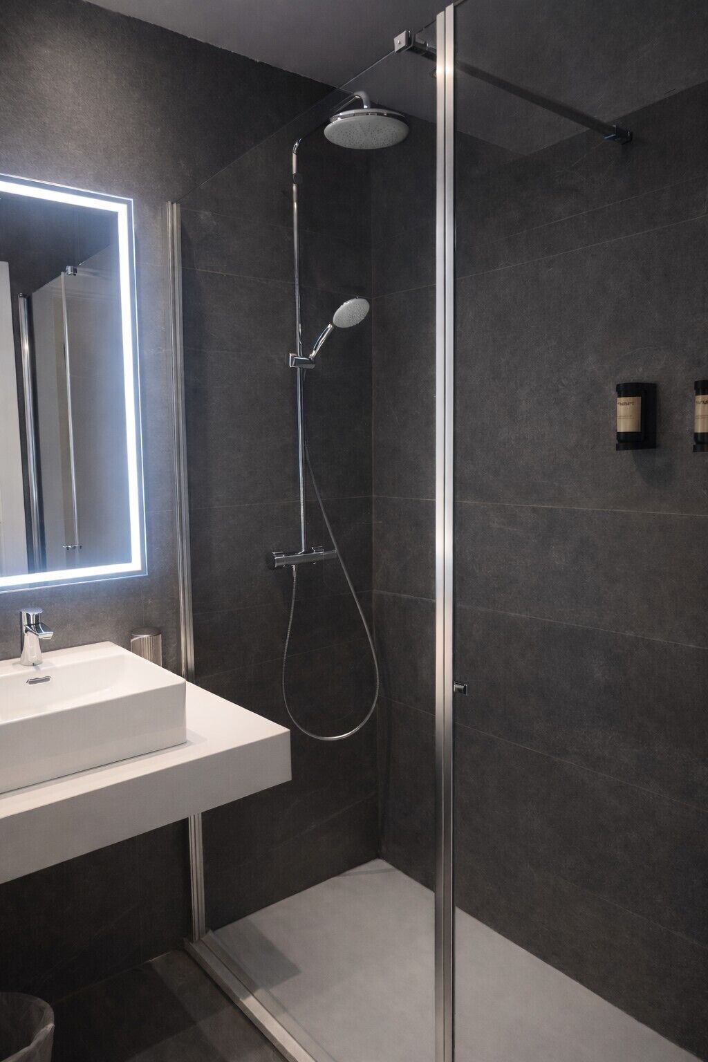 Une salle de bain moderne avec une douche à parois de verre, un lavabo blanc et un miroir doté d’un cadre éclairé.