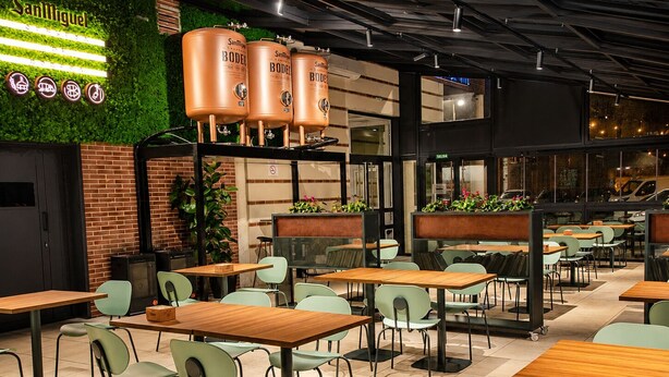 A restaurant with green chairs, wooden tables, and large copper beer tanks. - Hotel Andia (Orcoyen)