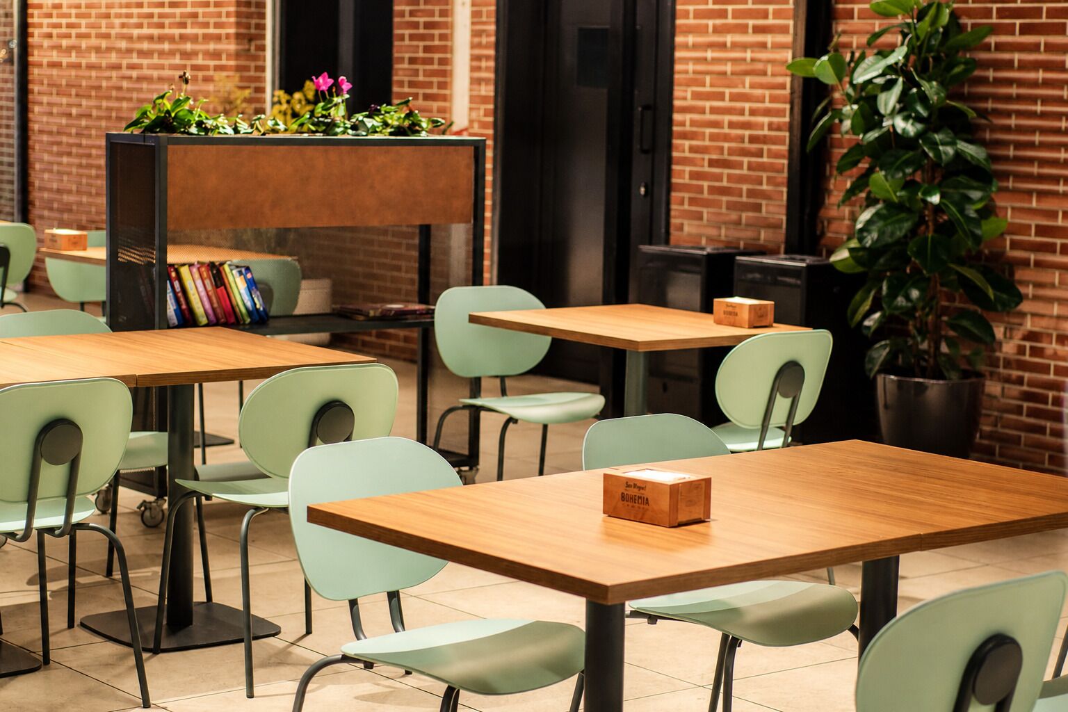 A café with tables and chairs, a bookshelf with books, and a potted plant.