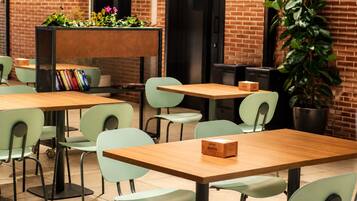 Una cafetería con mesas y sillas, una estantería llena de libros y una planta en maceta.
