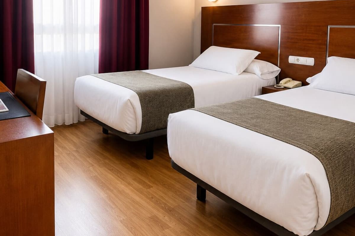 A hotel room with two beds, a desk, and a telephone.
