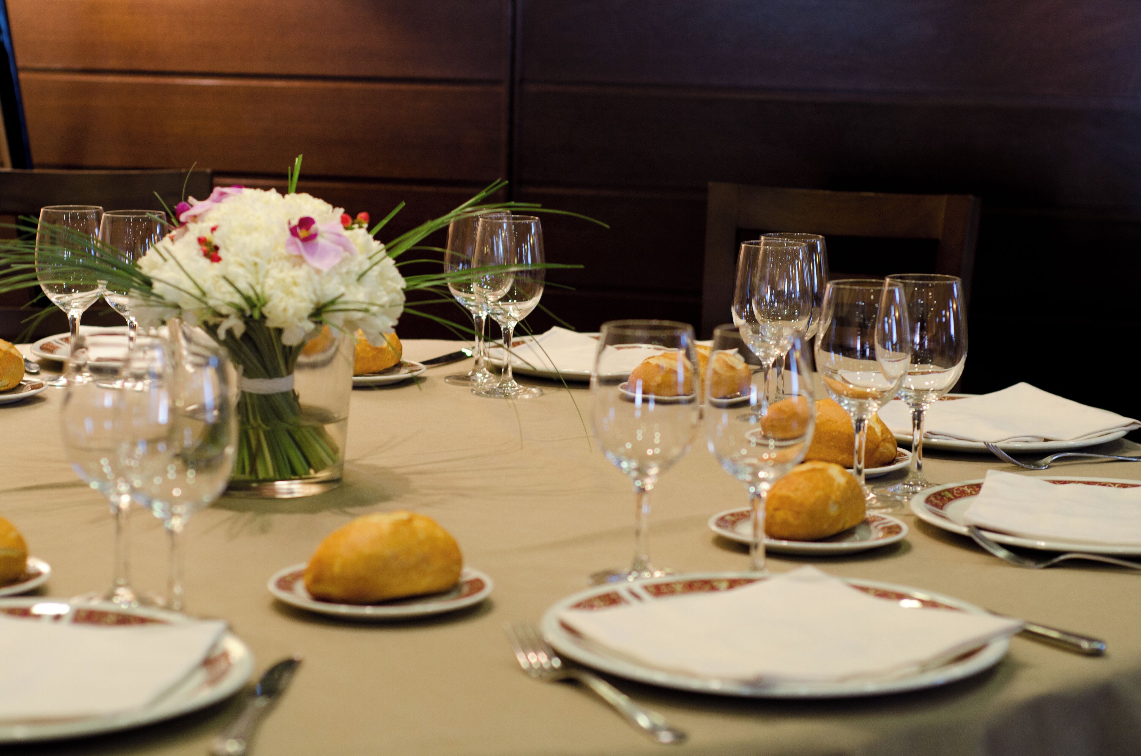 Una mesa servida para una comida, con platos, vasos y un florero con flores.