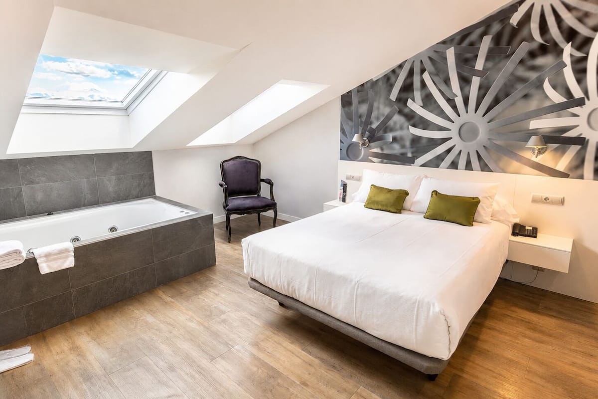 A modern bedroom with a skylight, a large bed, a bathtub, and a chair.