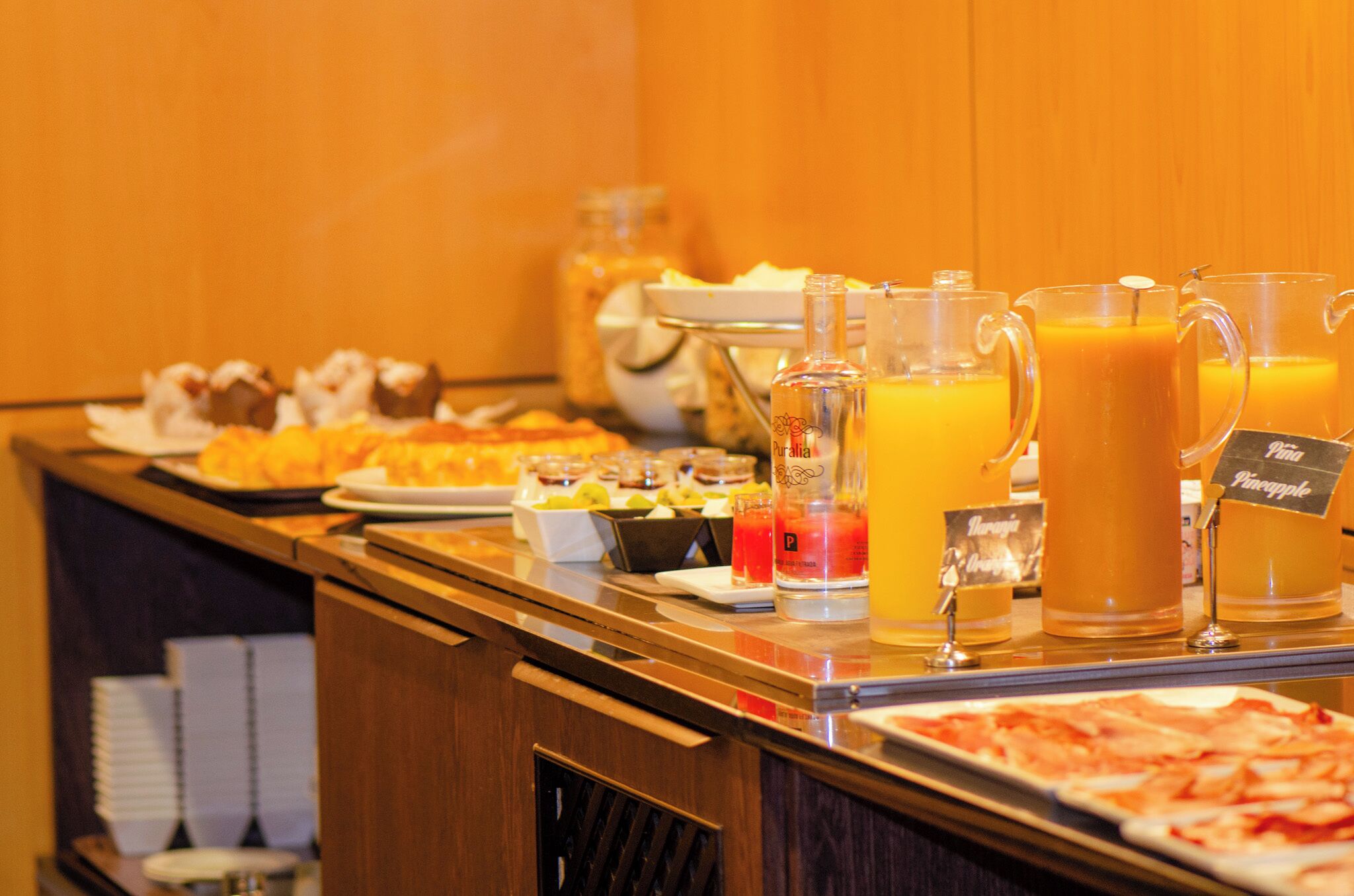 Un bufé con diversos alimentos y bebidas, entre ellos ponche de frutas y jugo.