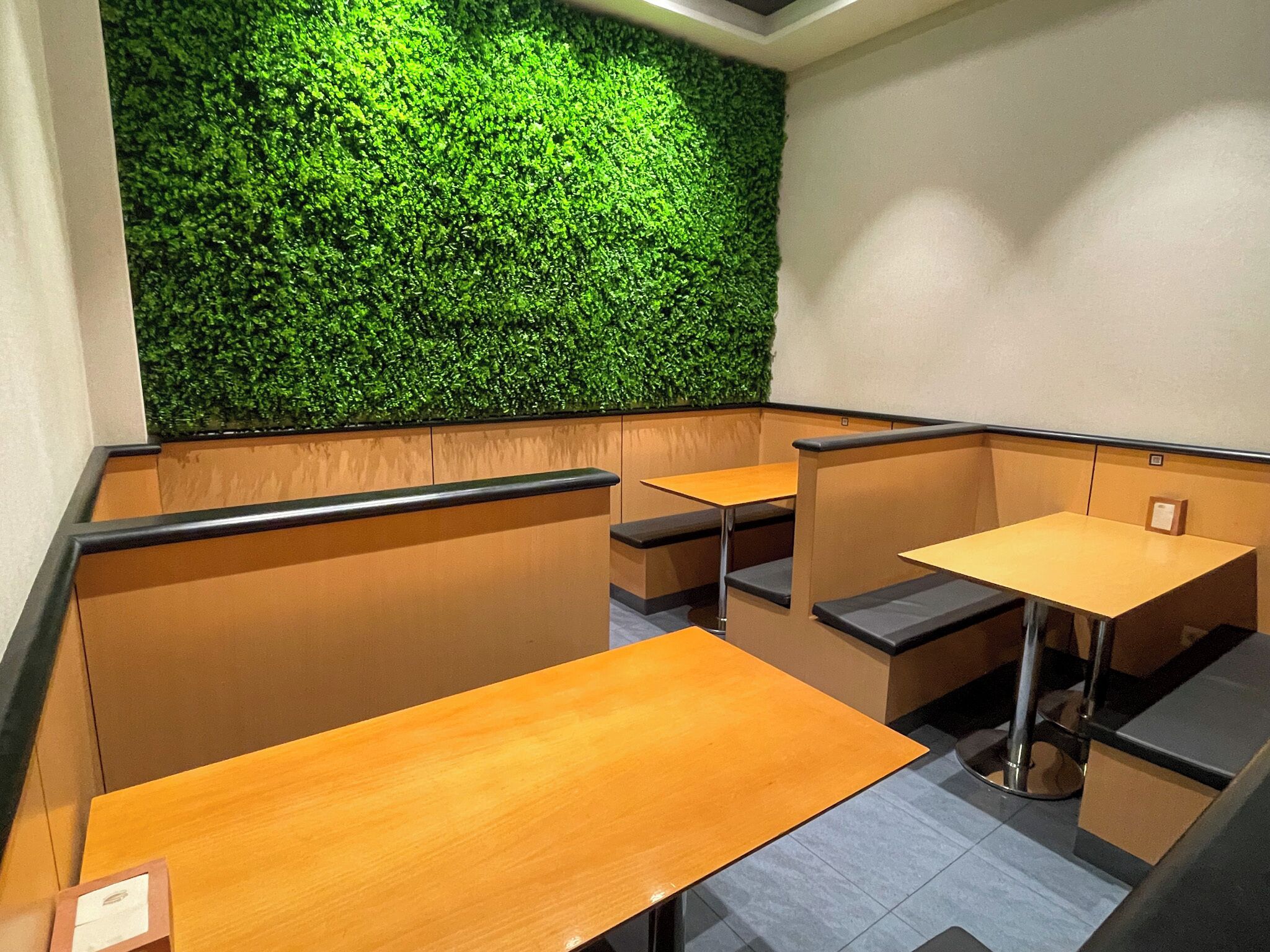 A modern interior with wooden tables and black cushioned seating, a green wall, and a ceiling light fixture.