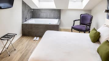 Un dormitorio con una cama grande, una silla, una mesita pequeña, una bañera y tragaluces.