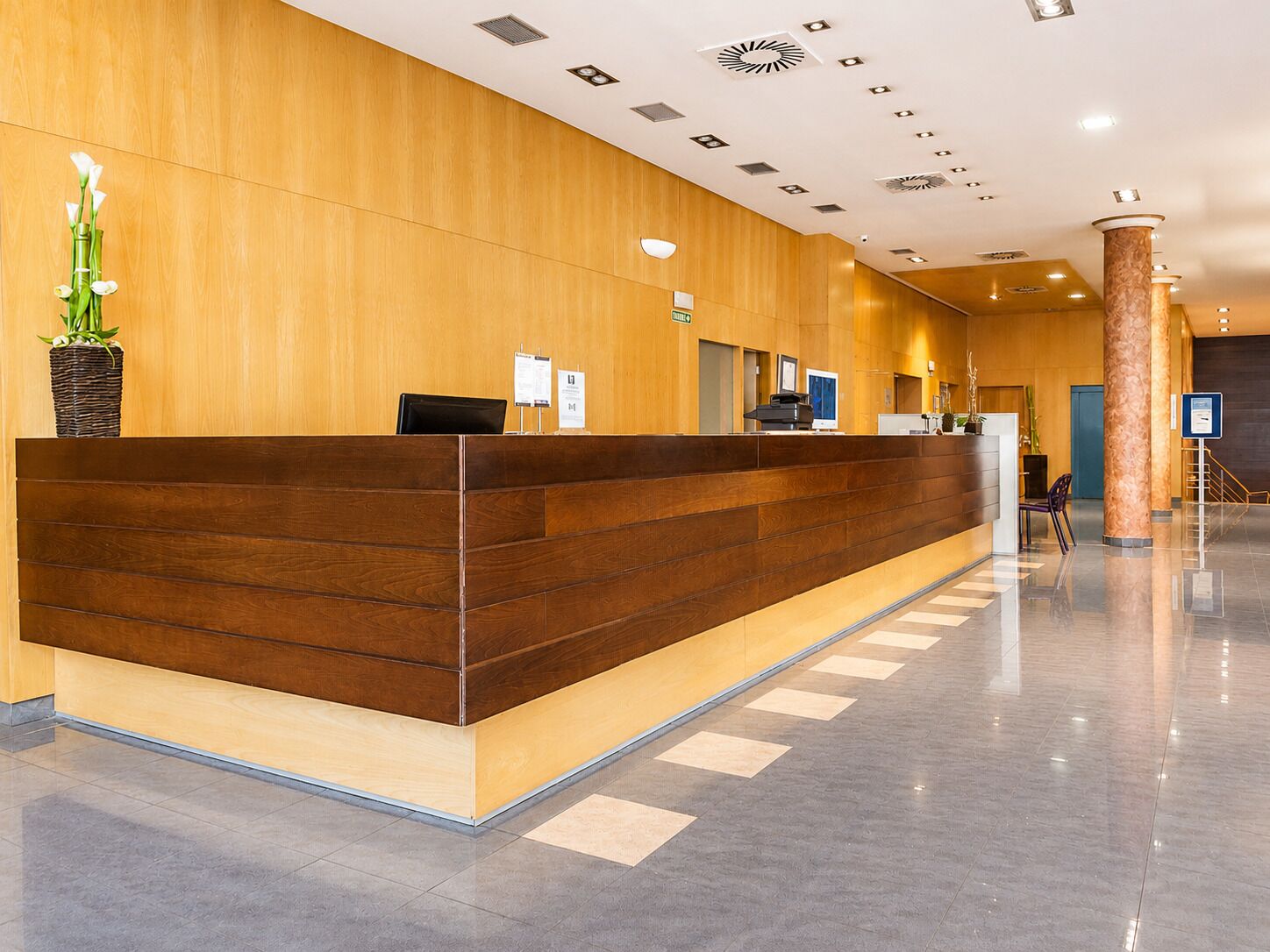 A reception desk with a wooden finish, a potted plant, and a sign indicating a waiting area.