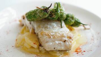 A white plate with a piece of white fish, green chili peppers, and a yellow sauce.