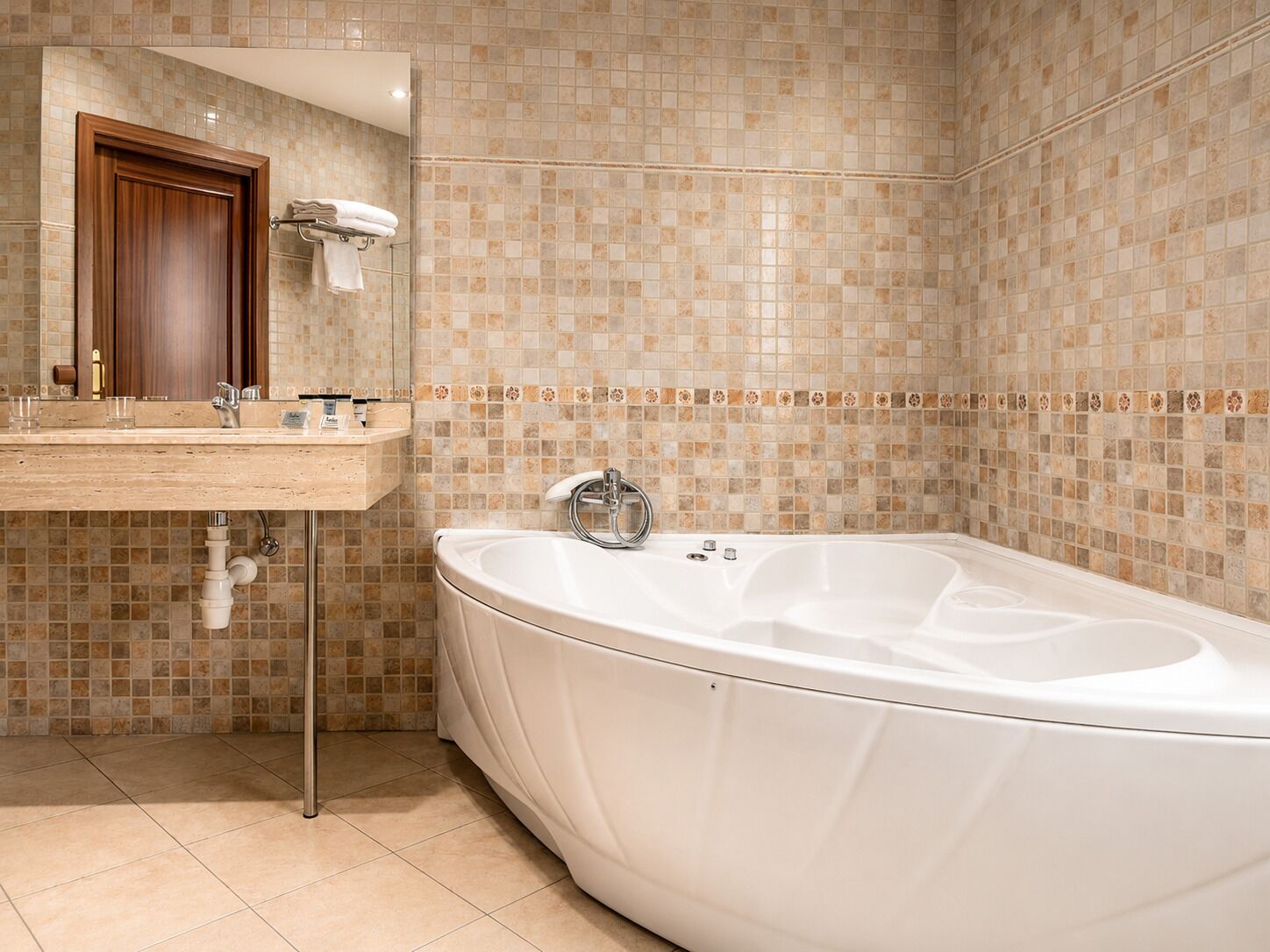 A bathroom with a large bathtub, a wooden vanity with a mirror, and tiled walls.