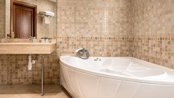 A bathroom with a large bathtub, a wooden vanity with a mirror, and tiled walls.