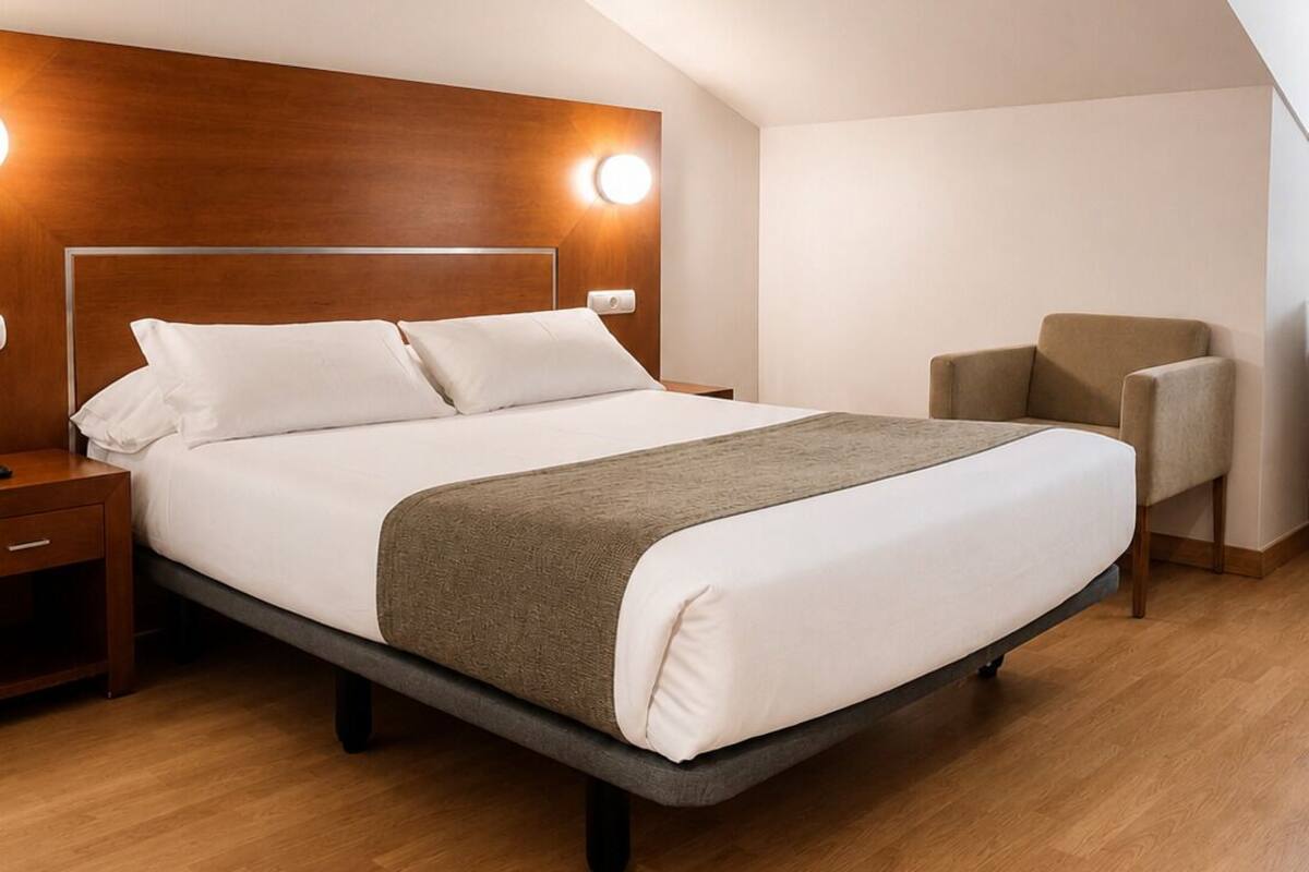 A modern bedroom with a wooden headboard, a bed with white bedding, a grey throw blanket, a nightstand, a chair, and a wooden floor.
