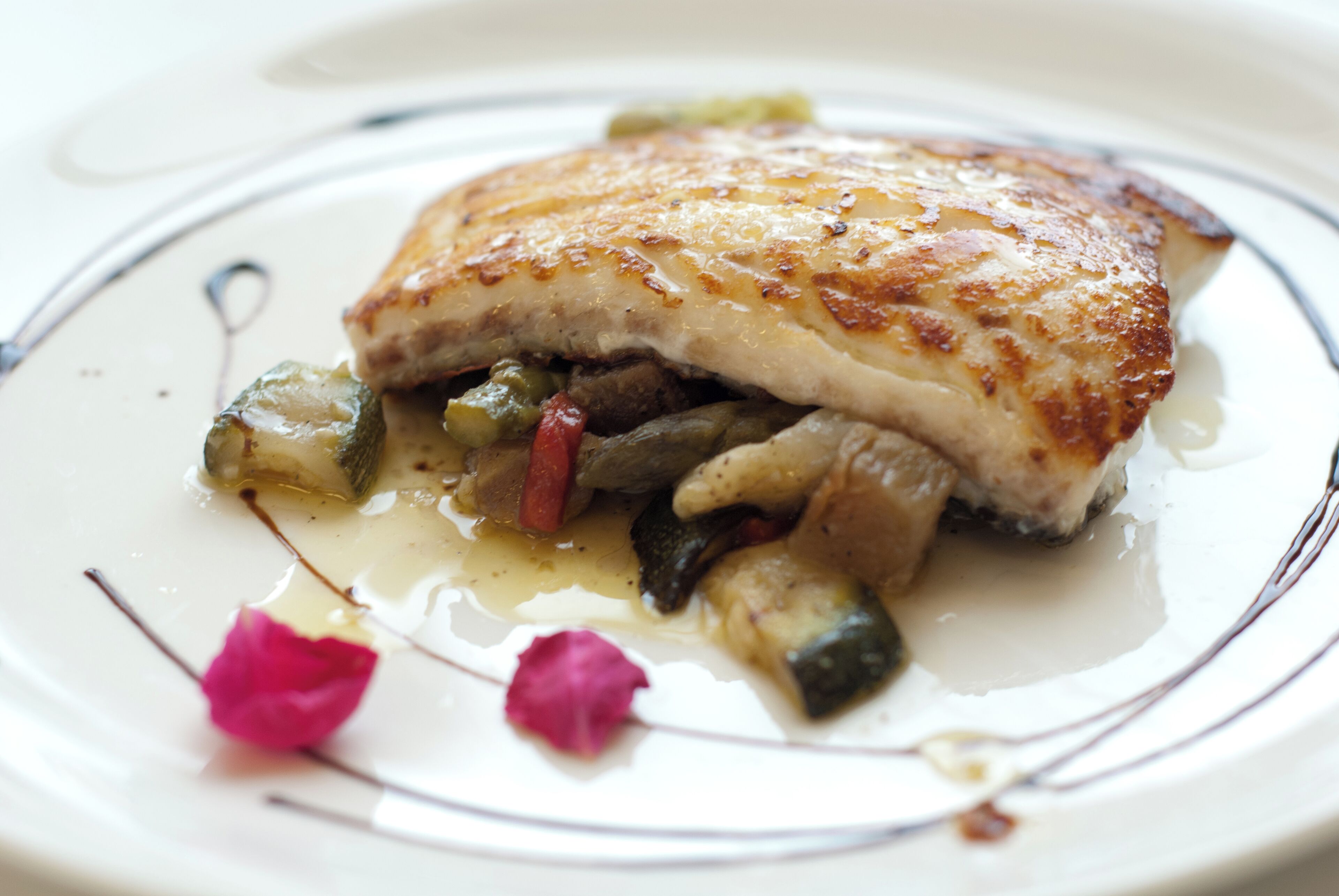 A plate with a piece of grilled chicken, vegetables, and a decorative flower.