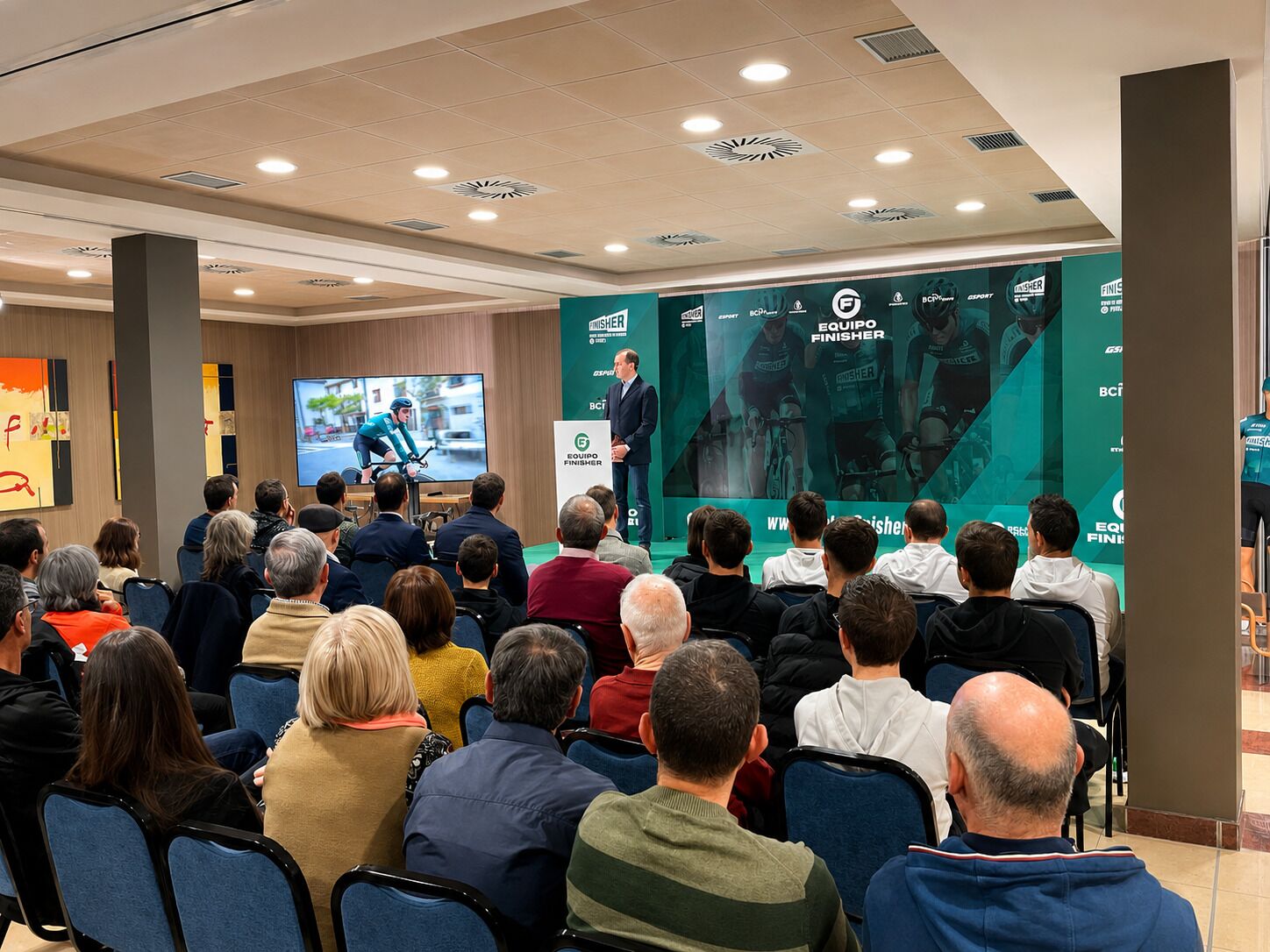 A conference room with a presentation screen, seated audience, and branded banners.