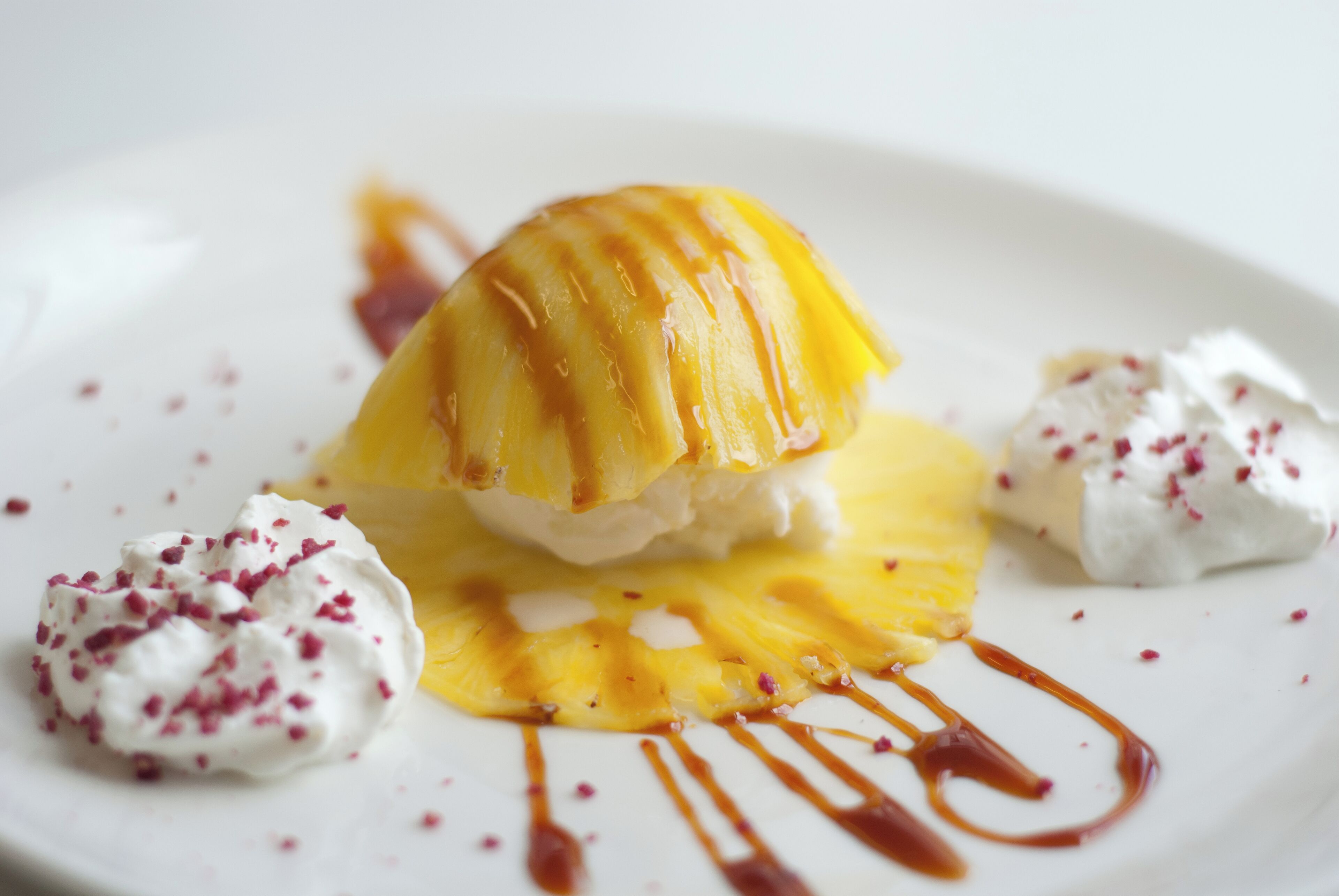 Un plato de postre con una rodaja de piña caramelizada, crema batida y un chorrito de salsa.