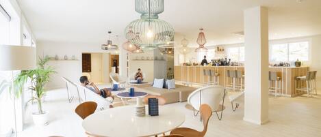 A spacious, well-lit dining area with a central round table, surrounded by wooden chairs, and a seating area with a sofa and chairs.
