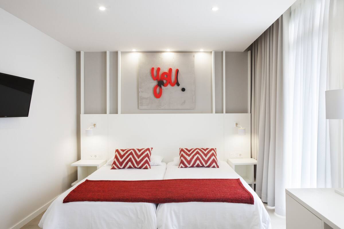 Een moderne hotelkamer met een groot bed, twee nachtkastjes, een flatscreen televisie en een kunstwerk aan de muur met de tekst 'you'.
