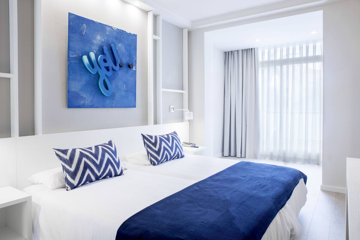 Een moderne hotelkamer met een groot bed, een blauw kunstwerk aan de muur en een raam met gordijnen.