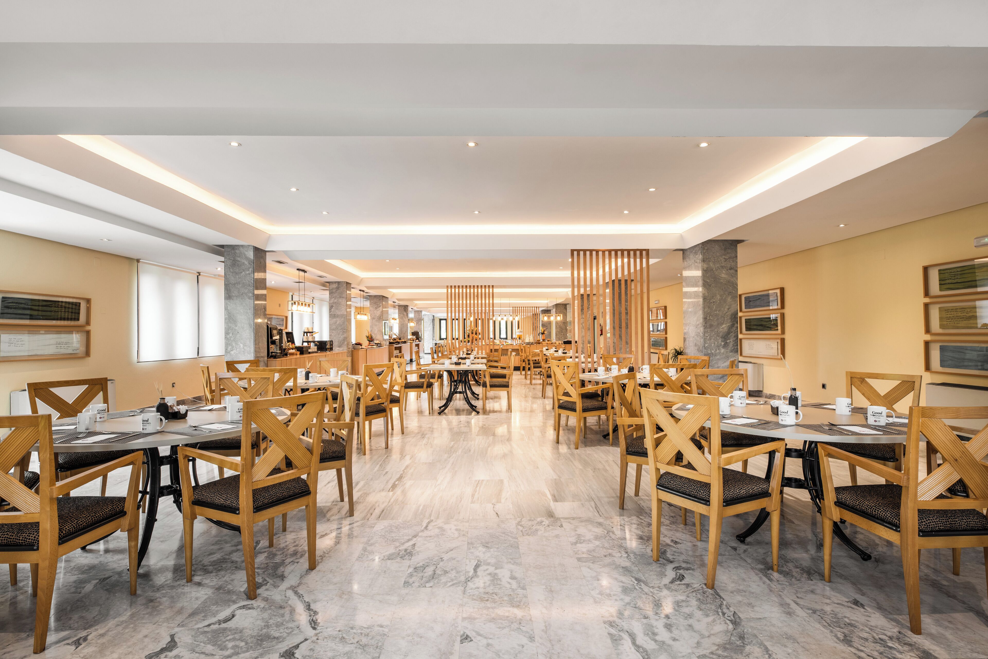A spacious dining area with multiple tables and chairs, marble flooring, and modern lighting fixtures.