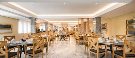 A spacious dining area with multiple tables and chairs, marble flooring, and modern lighting fixtures.