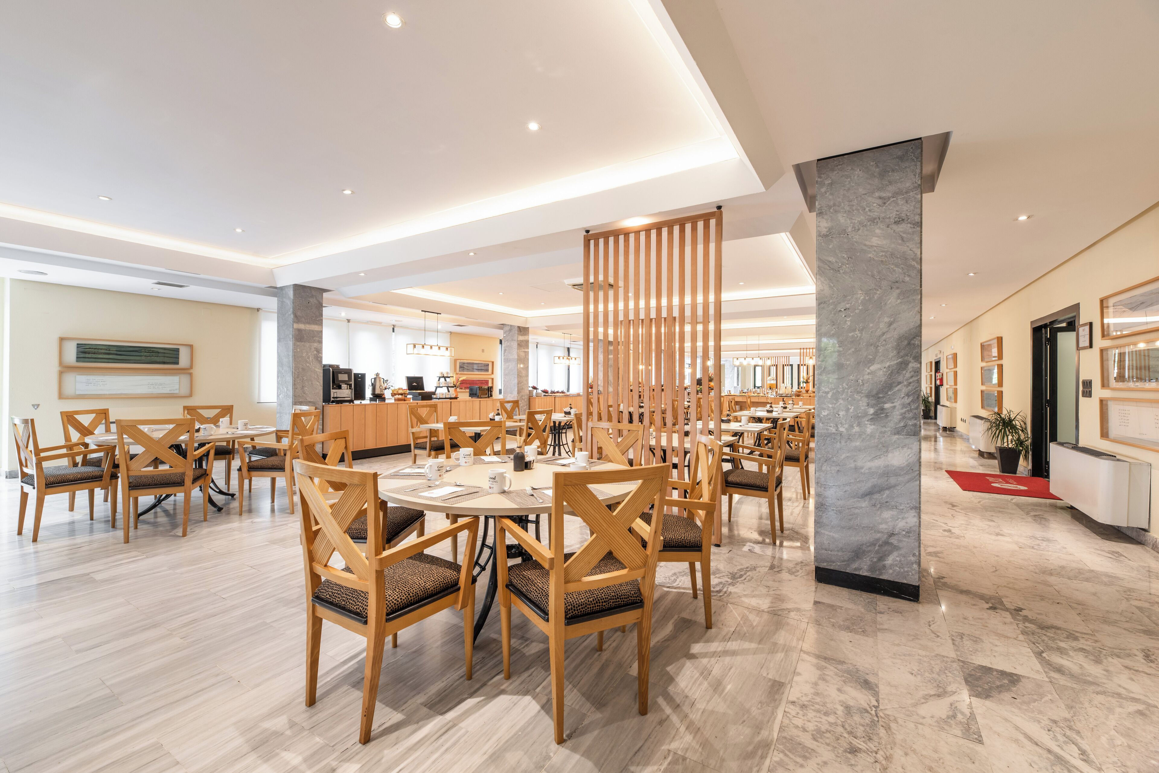A spacious dining area with wooden tables and chairs, a marble column, and a modern ceiling design.