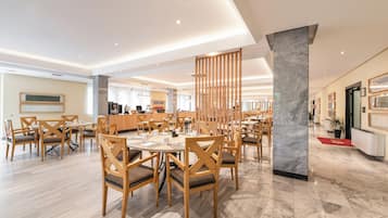 A spacious dining area with wooden tables and chairs, a marble column, and a modern ceiling design.
