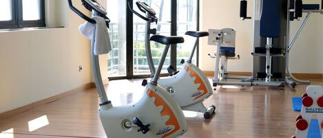 Un gimnasio con bicicletas estáticas, una máquina de pesas y una colchoneta azul.
