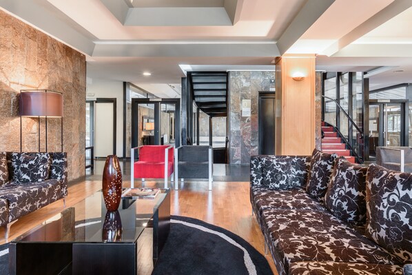 A spacious living area with a modern sofa, a red chair, and a coffee table. There is a staircase leading to an upper level. - EXE Auriense (Ourense)