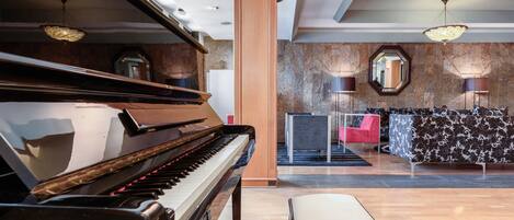 Un piano de cola en un vestíbulo amplio con una pared de mármol, un espejo grande y un sofá estampado.