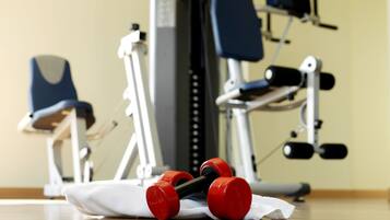 Een sportschool met trainingsapparatuur, waaronder gewichten en een bank.
