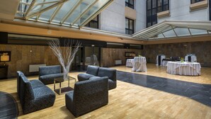 A spacious indoor area with a high ceiling and a glass roof, featuring a seating area with sofas and a central decorative piece. Tables are set up for dining in the background. - EXE Auriense (Ourense)