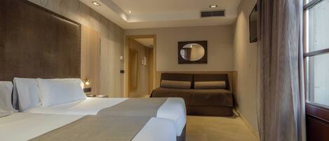 A hotel room with a large bed, a smaller bed, a sofa, a mirror, and a window with curtains.