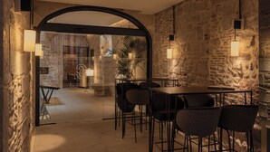 A modern interior with a stone wall, a glass door leading to a balcony, and a dining area with chairs and a table. - Gran Hotel Barcino (Barcelona)